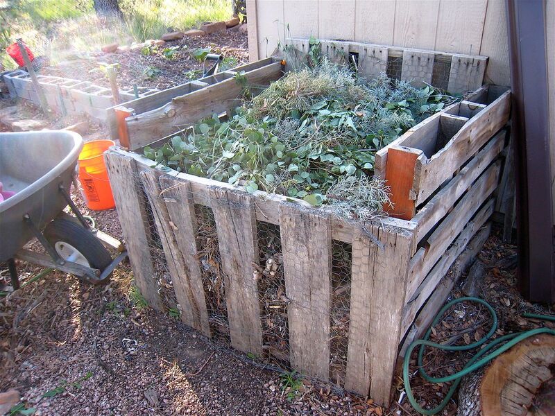 Rustic pallet compost bays heaped with fresh garden prunings beside a wheelbarrow